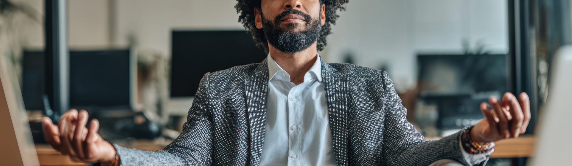 A professionally dressed man sits at a modern office desk, smiling while looking at his laptop, conveying a sense of focus and satisfaction.